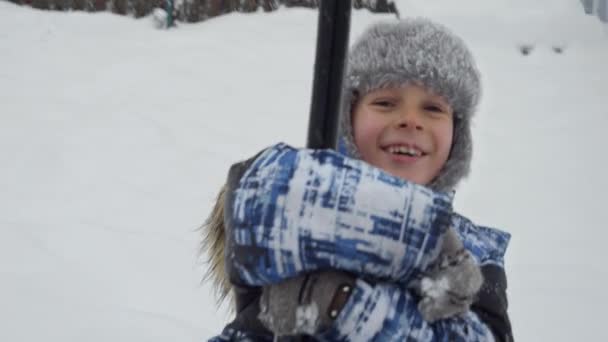 吹雪の後に雪に覆われた公共の遊び場でジップラインに乗る幸せな笑顔の少年 冬休みの楽しみと喜び 雪の中での活動 — ストック動画