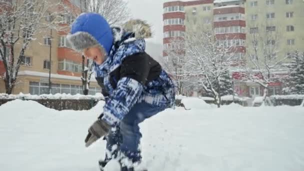 雪嵐や吹雪の後 遊び場で大きな雪のドリフトでジャンプ冬服の幸せな笑いの少年 冬休みの楽しみと喜び 雪の中での活動 — ストック動画