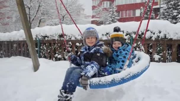 雪に覆われた遊び場でスイングする2人の兄弟としての冬の楽しさと笑い アウトドア活動と家族の楽しみ — ストック動画