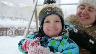 Parkta oynadıktan sonra küçük oğlundan kar silkeleyen genç bir anne. Kış tatillerinde eğlence ve neşe, dışarıda oynayan çocuklar, kar yağışında faaliyet