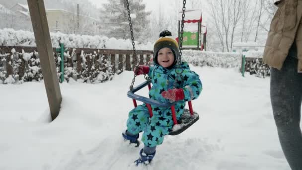 寒い冬の日に雪に覆われた公園で揺れ動く若い幼児の少年のスローモーション 子供のための冬の遊びの喜びと魔法を伝えるのに最適です — ストック動画