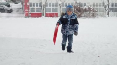 Karda plastikten kızaklarla koşan, temiz havanın ve kış manzarasının tadını çıkaran bir çocuk.