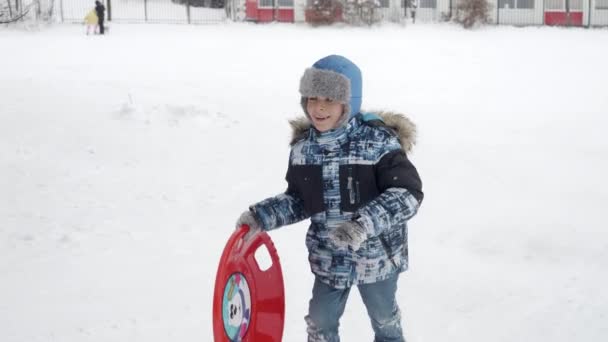 Ein Kleiner Junge Trägt Fröhlich Seine Schlitten Einen Schneebedeckten Hügel — Stockvideo