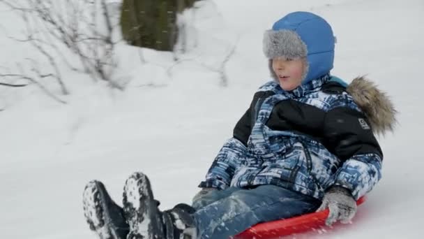 一个小男孩慢吞吞地沿着雪山飞驰而下 跳上他塑料雪橇上的蹦床 寒假的魔力和童年游戏的欢乐 — 图库视频影像