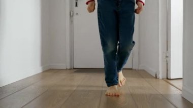 Evinin uzun ahşap koridorunda koşan küçük bir çocuğun ayakları yavaş hareket ediyor. Mutlu çocukluk, kapalı mekan oyunları ve bir çocuğun gelişimsel becerilerinin gelişimi.