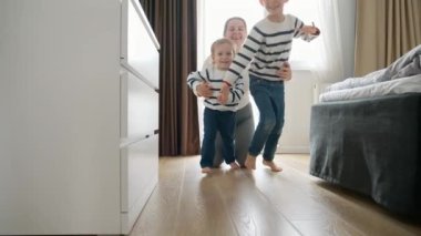 Evdeki uzun ahşap koridorda koşan iki küçük çocuğun yavaş çekim görüntüsü. Mutlu bir çocukluk kavramı, kapalı alanlarda oynamak, ve bir çocuğun fiziksel ve motor becerilerinin gelişimi ve gelişimi