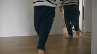 Evdeki ahşap zeminde koşan iki küçük çocuğun ve annelerinin ayakları. Mutlu ve neşeli bir ailenin birlikte vakit geçirmesi kavramı.