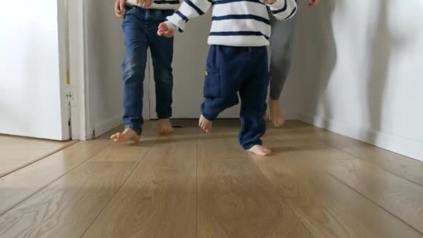 顽皮的小男孩和他们的母亲的脚在家里的木地板上跑着 一个温馨的家庭之爱和快乐童年回忆的概念 — 图库视频影像
