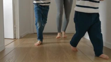 Evdeki ahşap zeminde koşan bir anne ve iki çocuğun yavaş çekim görüntüleri. Aile bağları, neşe ve neşe