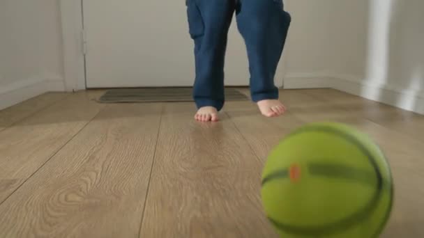 幼い少年の足がゆっくりと動き 家の長い廊下の木製の床の上でボールで遊んでいます 幼児期の発達 屋内遊び 楽しい探検の概念 — ストック動画