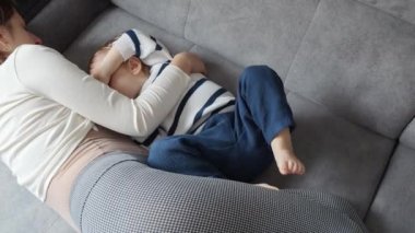 Anne, bebeğini kanepede sıcak ve rahat bir ortamda emziriyor. Anne bakımı kavramı, çocuk gelişimi ve emzirmenin önemi