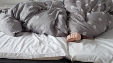 Yatakta sarmaş dolaş yatarken battaniyenin altından çift ayakları görünüyor. Samimiyet, birliktelik ve memnuniyet kavramı.