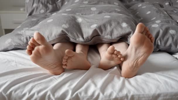 有爱心的父母和孩子的脚踏在毯子下躺在床上 家庭之爱 快乐的童年 一起在家里玩乐 养育子女 恋爱关系和家庭生活的概念 — 图库视频影像