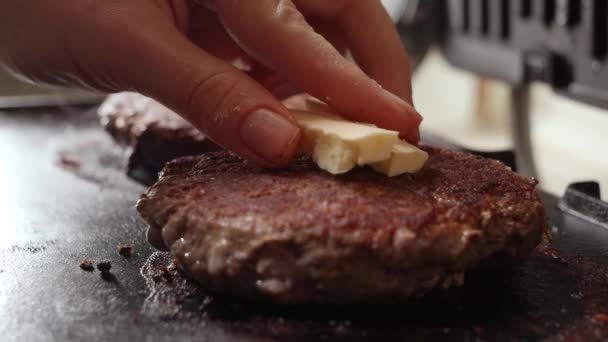 手を閉じるグリル上のローストビーフバーガーパテにバターを入れて 家庭での調理 キッチン家電 健康的な栄養 ハンバーガーの成分 — ストック動画