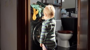Küçük bebek çamaşır makinesinin düğmelerine ve düğmelerine basıyor. Ev işleri ve ev işleri, çocukların eğitimi ve gelişimi.
