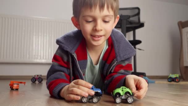 一个可爱的男孩躺在地板上玩两辆玩具车的肖像 儿童独自玩耍 发展和教育 家庭游戏 — 图库视频影像