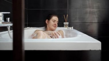 Köpük ve köpüklerle banyoda dinlenen zarif bir kadın resmi. Kadın hijyeni, banyoda dinlenme, güzellik ve sağlık.