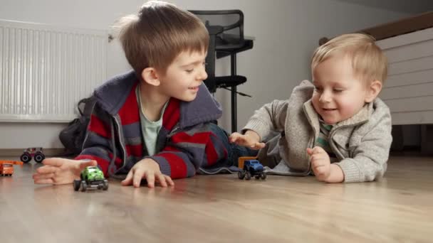 床におもちゃの車のレースを持っている兄と赤ちゃんの男の子 一人で遊ぶ子供たち 開発と教育 家庭でのゲーム — ストック動画