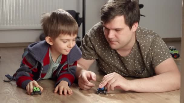 床におもちゃの車で父親と遊んでいる男の子 一人で遊ぶ子供たち 開発と教育 家庭でのゲーム — ストック動画
