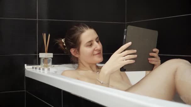 女性はリラックスしたお風呂に入り タブレットコンピュータで自分自身を楽しませます 近代的な技術 リモートジョブで働く — ストック動画