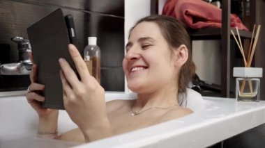 Tablet bilgisayarında arkadaşları ya da ailesiyle görüntülü konuşma yaparken banyoda dinlenen bir kadın. Modern yöntemlerle kişisel bakım ve sosyal etkileşimi dengeleriz.