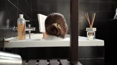 İlginç bir kitapla banyoda rahatlayan zarif bir kadının arka görüntüsü. Kişisel bakım, eğitim, hijyen ve kaplıca