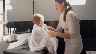 Duşta yıkandıktan sonra banyo havlusuyla kaplı bebeğinin saçını tarayan genç bir anne. Ebeveynlik, mutluluk ve çocuk hijyeni kavramı