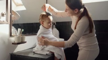 Mutlu gülümseyen anne banyoda yıkandıktan sonra saçlarını saç fırçasıyla tarıyor. Ebeveynlik, mutluluk ve çocuk hijyeni kavramı