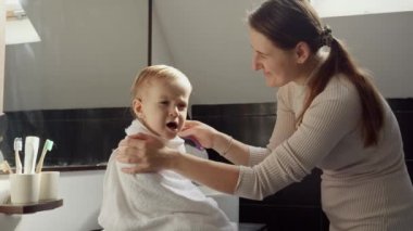 Mutlu gülümseyen anne, bebeğini havluyla silerek saçlarını tarıyor. Ebeveynlik, mutluluk ve çocuk hijyeni kavramı