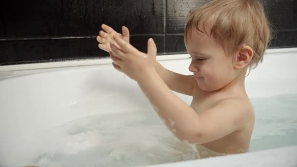 一个小男孩在他的浴室里咯咯地笑着 溅起水花 形成了水花 纯真的幸福和童年的无忧无虑 — 图库视频影像