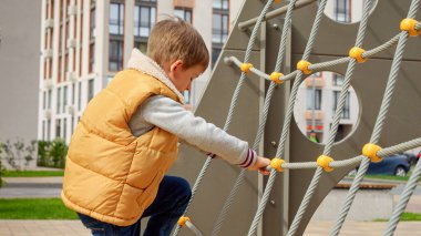 Halat ve ağlarla halk parkında oynayan ve yükseğe tırmanan mutlu aktif çocuk. Aktif çocuk, spor ve gelişim, açık havada oynayan çocuklar..