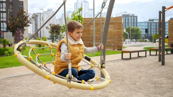Mały Chłopiec Cieszący Się Huśtawką Sieci Nowoczesnym Publicznym Placu Zabaw — Zdjęcie stockowe