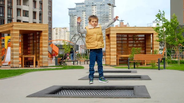 Yeni inşa edilmiş halk parkında trambolinde zıplayan mutlu gülen çocuk. Aktif çocuk, spor ve gelişim, açık havada oynayan çocuklar..