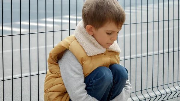 Zdenerwowany Samotny Chłopiec Zastraszany Szkole Siedzący Obok Metalowego Ogrodzenia Placu — Zdjęcie stockowe