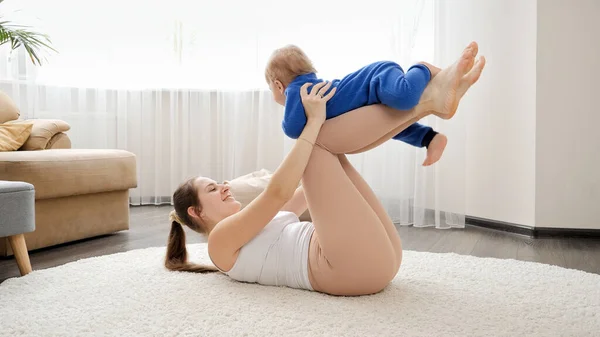 幸せな若い女性が床に伸ばし 彼女の赤ちゃんの息子と遊ぶ 家族の健康 積極的なライフスタイル 子育てと子供の発達 — ストック写真