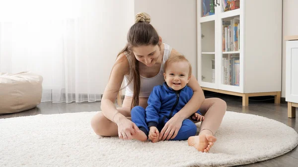 漂亮的年轻妈妈在家里的地毯上为她一岁的小儿子做伸展和按摩 — 图库照片
