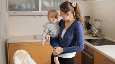 Little baby boy crying and screaming while mother seating him in feeding highchair on kitchen. Concept of parenting, healthy nutrition and baby care