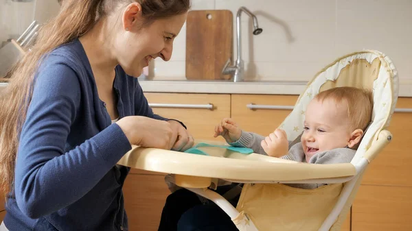 幸せな笑い母とともに赤ちゃん息子座っています上の椅子にキッチン — ストック写真