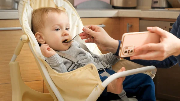 Mother Showing Video Smartphone While Feeding Her Baby Highchair Concept —  Fotos de Stock
