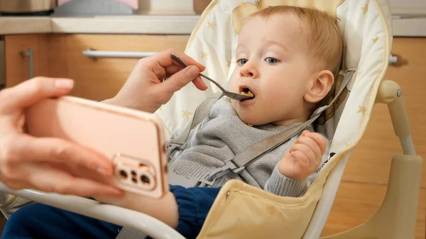 Portrait Cute Baby Boy Eating Porridge Highchair Watching Cartoons Smartphone — Stock Photo, Image