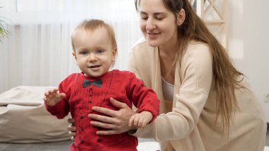Gülümseyen tatlı çocuk, genç annesiyle yürümeyi öğreniyor. Bebek gelişimi, aile oyunları, ilk adımlar, ebeveynlik ve bakım.