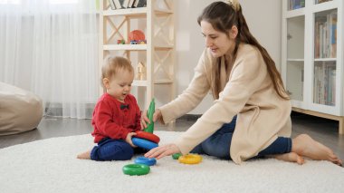 Güzel, genç bir anne, küçük oğluyla yerde oynuyor ve oyuncak kulesi kuruyor. Bebek gelişimi, çocuk oyunları, eğitim ve öğrenim