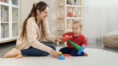 Genç bir kadın renkli yüzüklerle oyuncak kulesi yapmasına yardım ediyor. Bebek gelişimi, çocuk oyunları, eğitim ve öğrenim