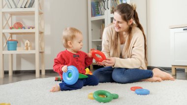 Evde yumuşak halıya çocuk oyuncağı kulesi inşa eden mutlu bir anne. Bebek gelişimi, çocuk oyunları, eğitim ve öğrenim