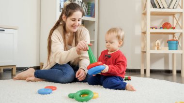 Annesiyle mutlu bir bebek oturma odasında renkli oyuncaklarla oynuyor..