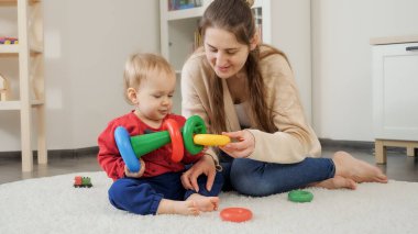Küçük oğluna renkli oyuncak piramidi yapmayı öğreten genç bir anne. Bebek gelişimi, çocuk oyunları, eğitim ve öğrenim