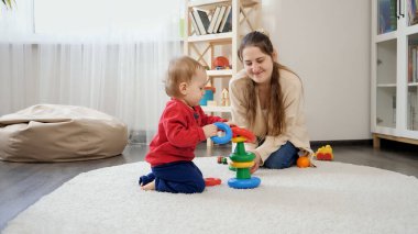 Annesiyle birlikte eğitici oyuncaklarla oynayan ve renkli kule yapmayı öğrenen küçük bir çocuk. Bebek gelişimi, çocuk oyunları, eğitim ve öğrenim