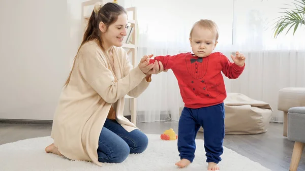 Sorrindo Jovem Apoio Segurando Seu Filho Bebê Aprendendo Andar Tapete — Fotografia de Stock