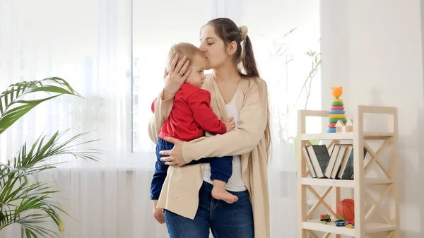 Milující Mladá Matka Drží Svého Malého Syna Líbá Čele Doma — Stock fotografie