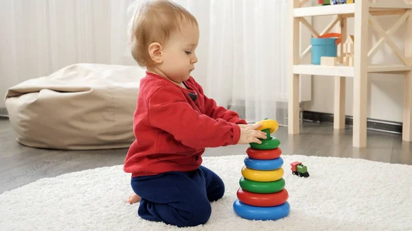 Little baby assembling to tower or pyramid on the floor at home. Baby development, child playing games, education and learning